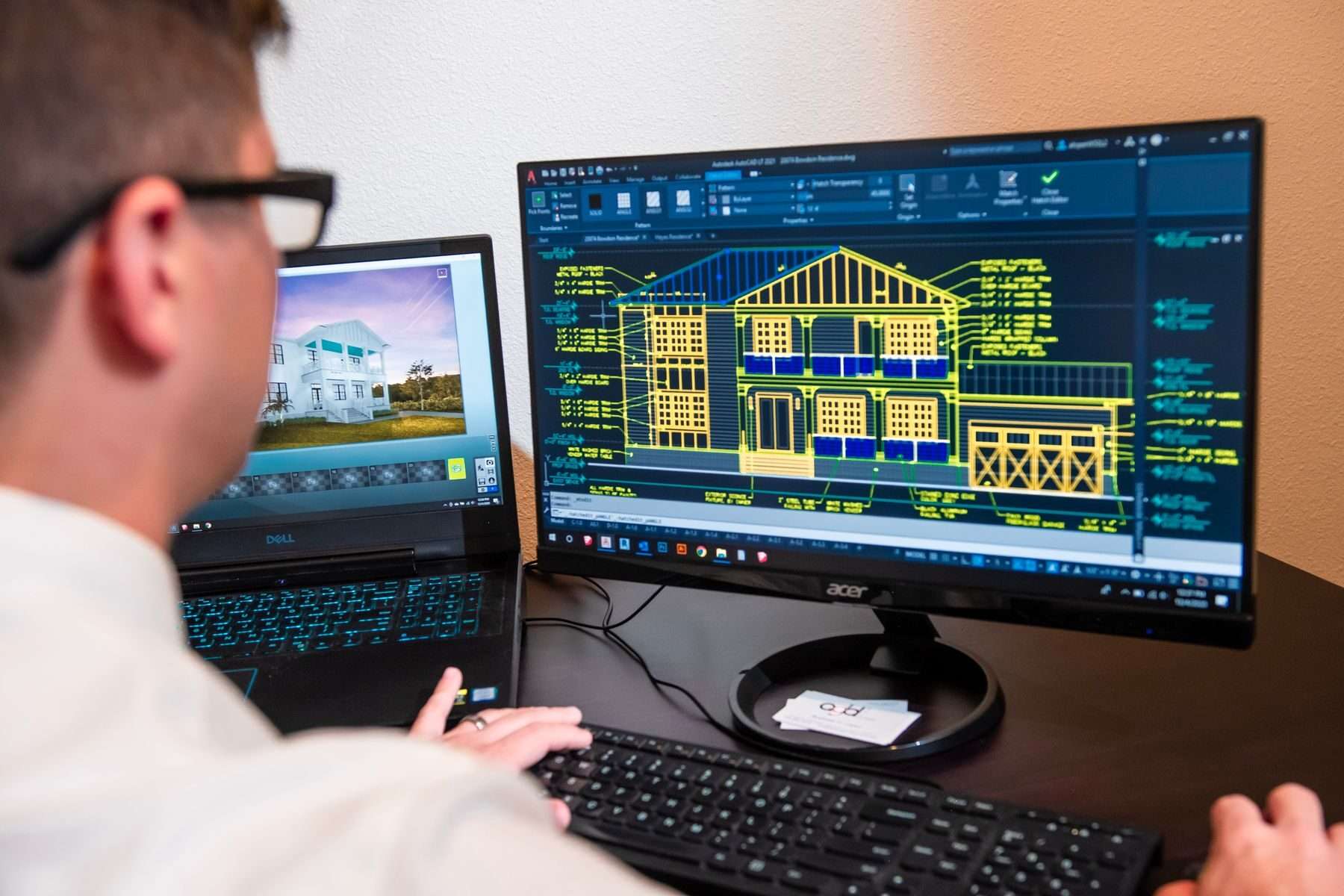 Konstrukteur zeichnet am Bildschirm im CAD die Ansicht eines Wohnhauses, auf dem Laptop daneben die Visualisierung.