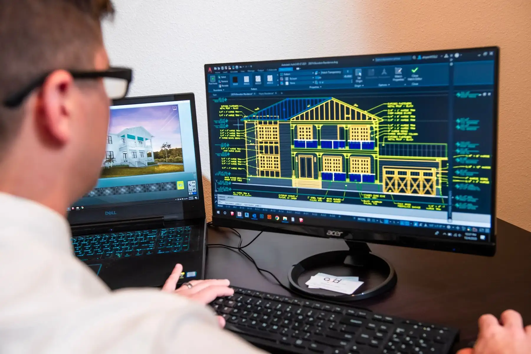 Konstrukteur zeichnet am Bildschirm im CAD die Ansicht eines Wohnhauses, auf dem Laptop daneben die Visualisierung.
