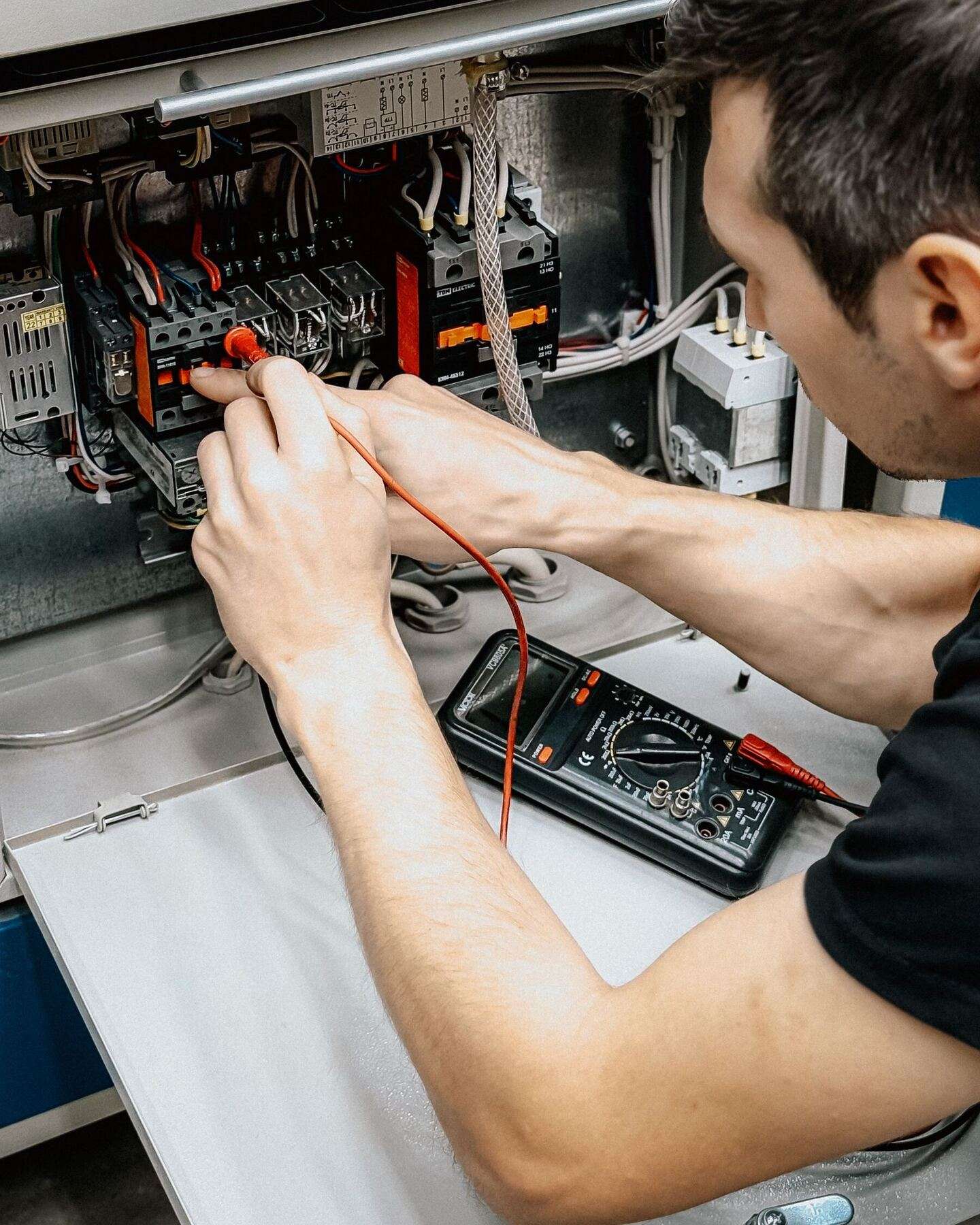 Elektroniker misst mit einem Multimeter an Klemmen und Schützen in einem geöffneten Schaltschrank einer Maschine.