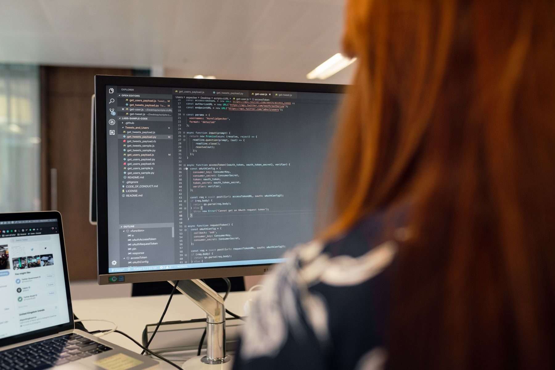 Entwicklerin von hinten am Arbeitsplatz, auf dem Bildschirm Quellcode im Editor.