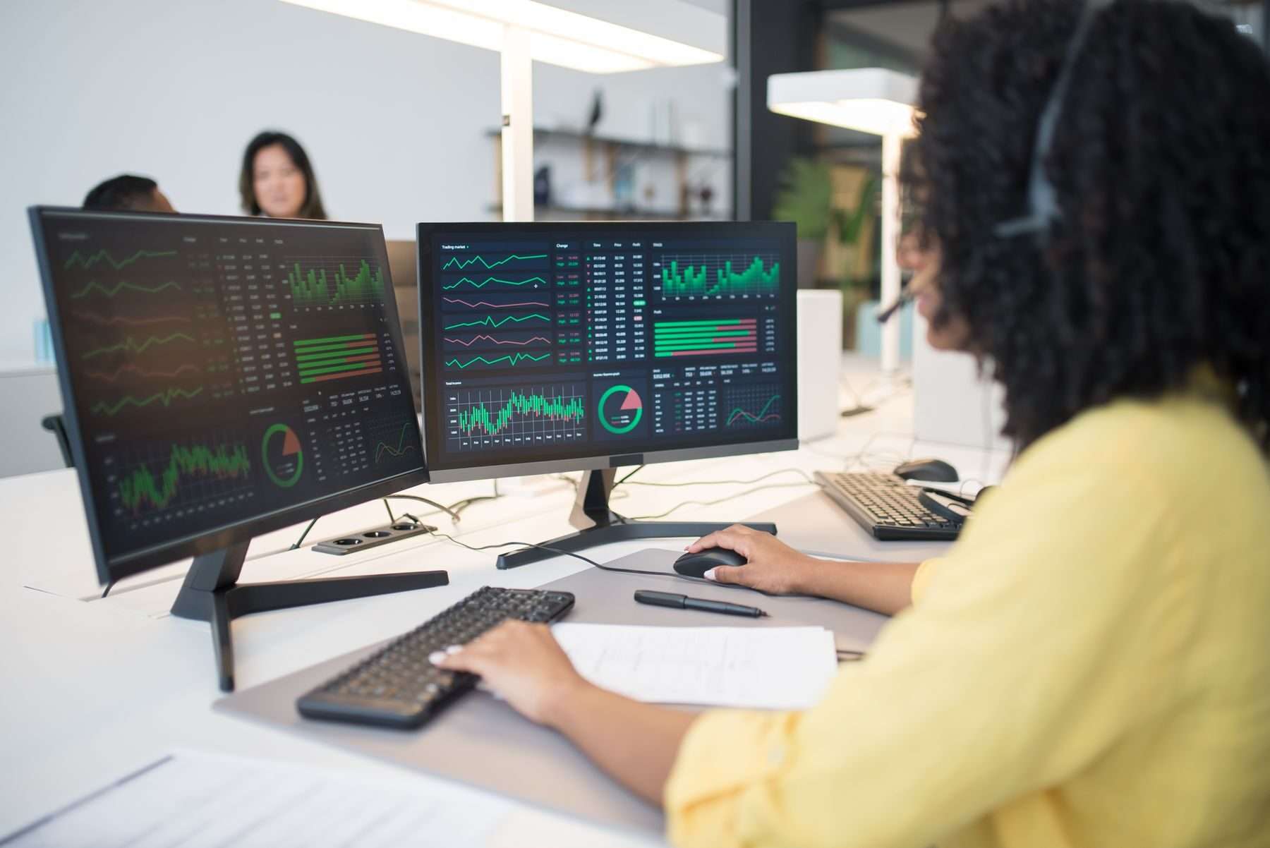 Mitarbeiterin mit Headset arbeitet an zwei Bildschirmen mit Diagrammen und Kennzahlen.