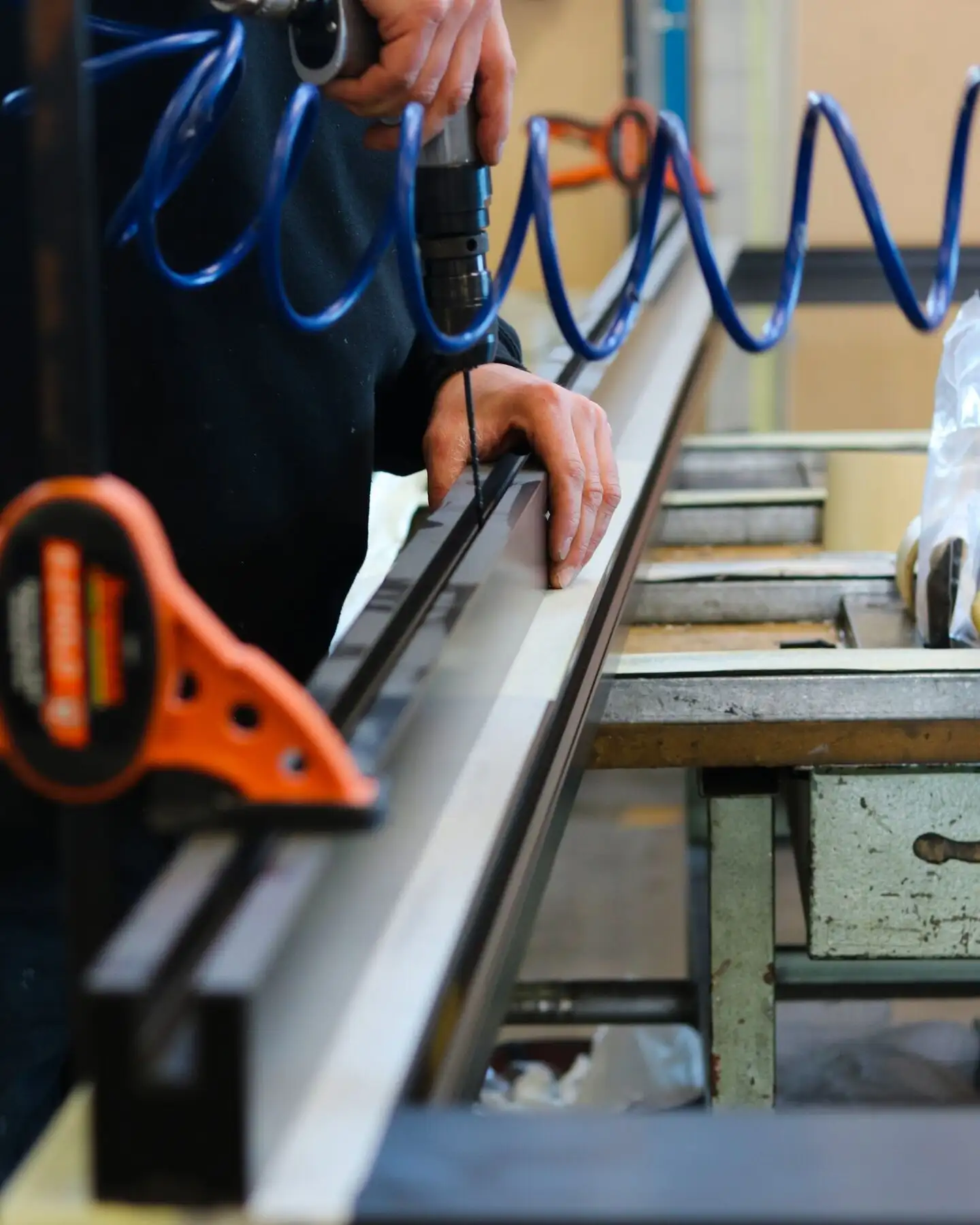 Monteur hält ein Aluminiumprofil am Werktisch und schraubt mit einem Druckluftschrauber, Spiralschlauch im Hintergrund.