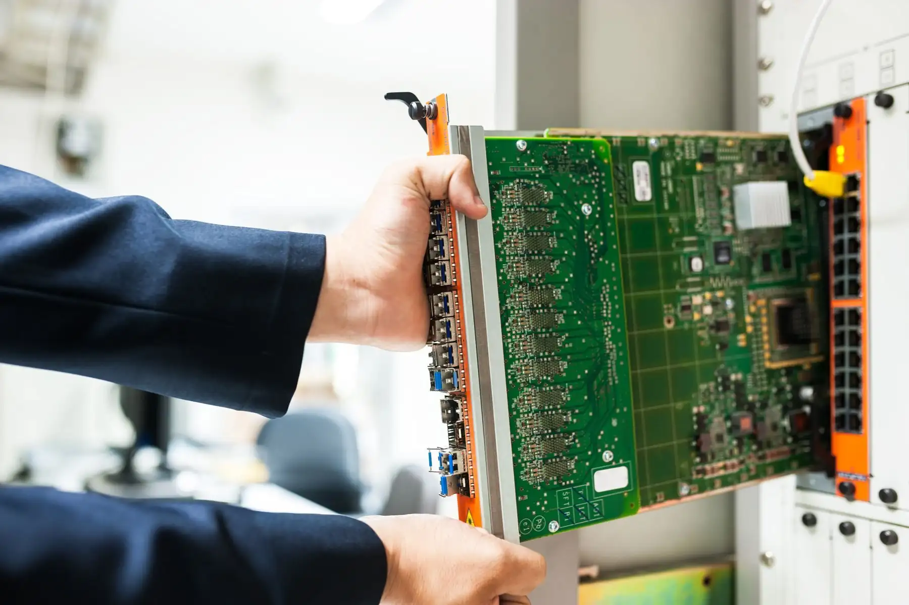 Hände schieben eine Netzwerk-Steckkarte in einen Baugruppenträger im Technikraum.