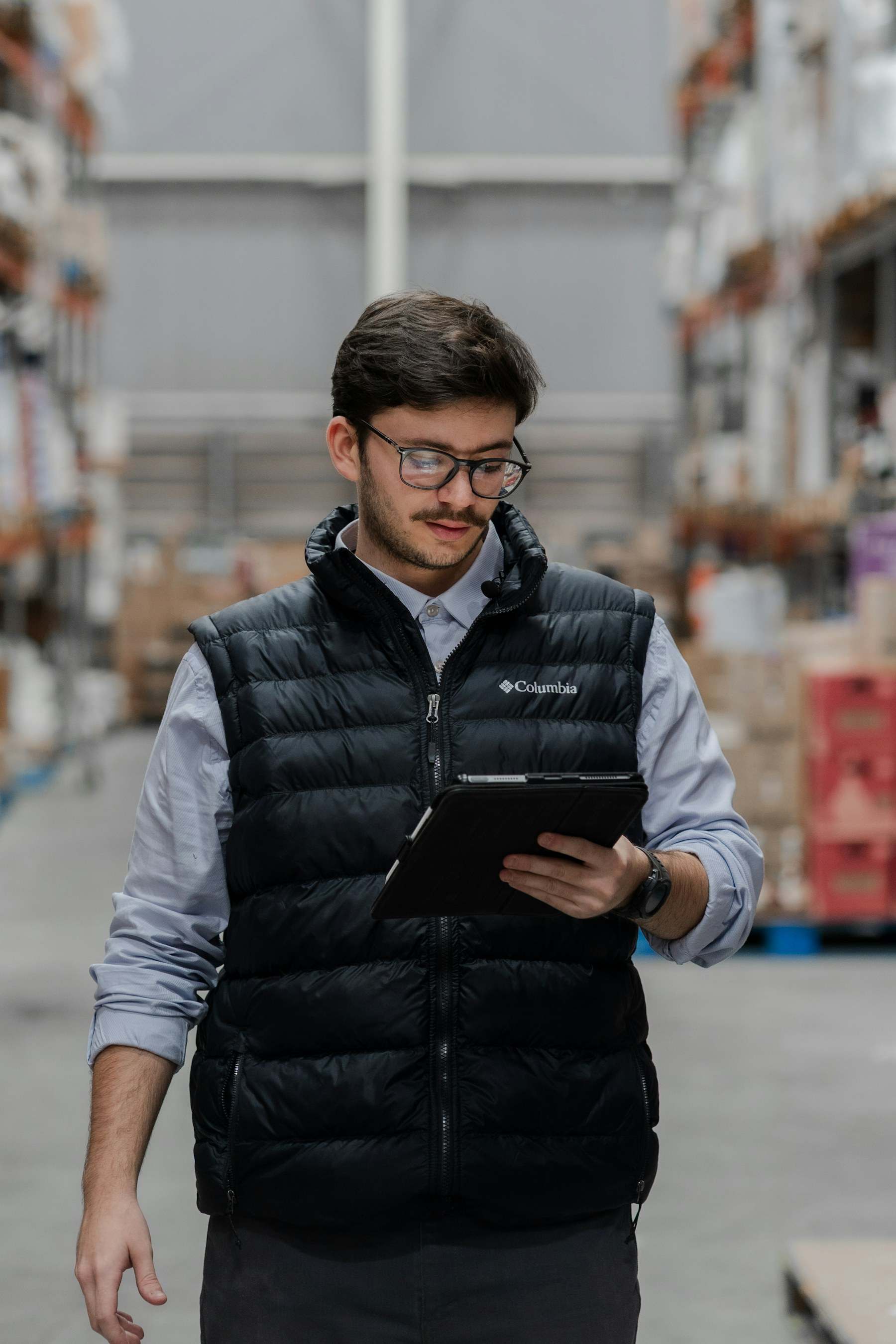Junger Mitarbeiter mit Tablet zwischen Regalen im Lager