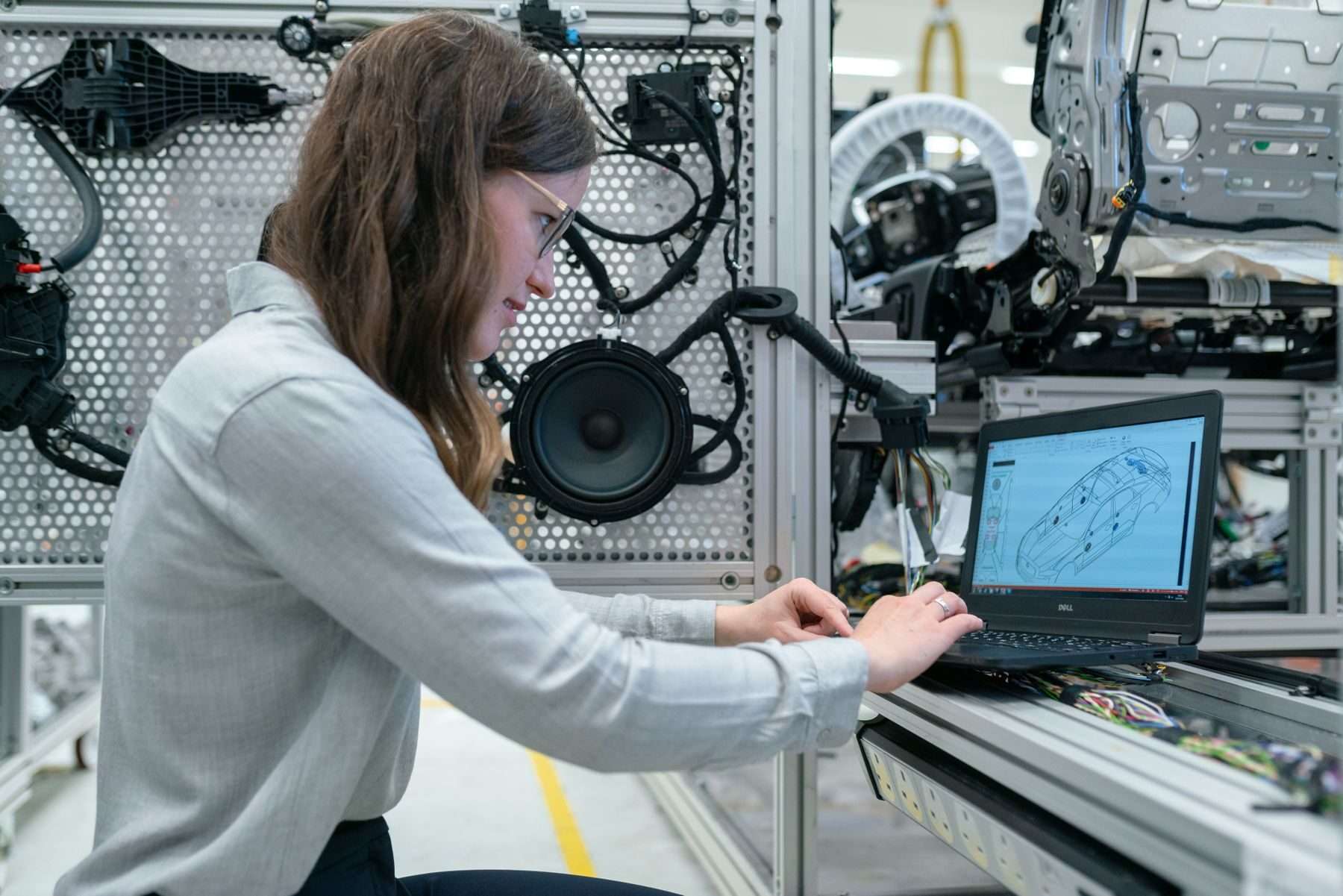 Junge Technikerin programmiert am Laptop eine Prüfanlage aus Aluminiumprofilen mit Kabelbäumen, Sensoren und Baugruppen.
