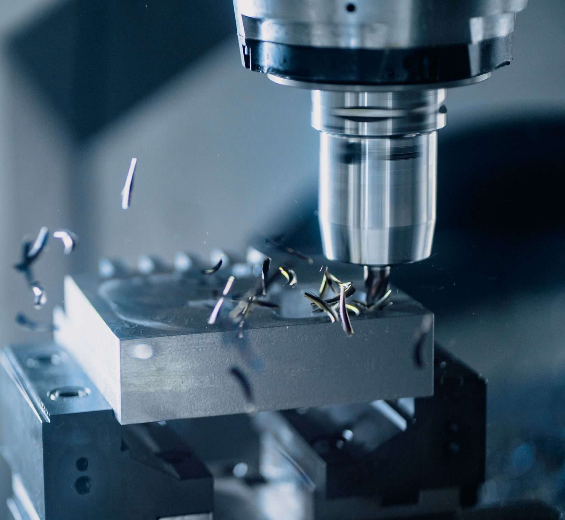 Schaftfräser einer CNC-Fräsmaschine fräst einen im Schraubstock gespannten Stahlblock, Späne fliegen.
